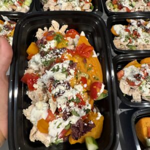 black plastic container with food in it, chicken, cheese, and vegetables